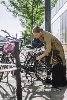 Geschäftsfrau, die ihr Fahrrad aufschließt, während sie an einer Parkstation steht - MASF33903