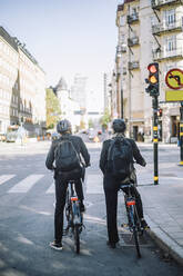 Rear view of business colleagues with bicycles waiting at traffic signal - MASF33905