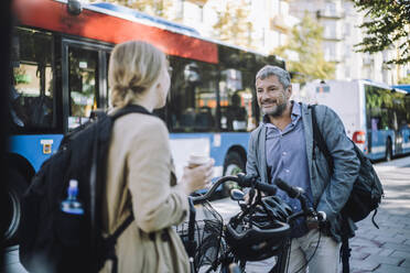 Male and female business colleagues with bicycles talking to each other at street - MASF33912