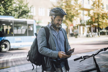 Smiling businessman wearing cycling helmet using mobile phone - MASF33913