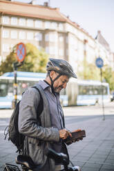 Mature businessman using smart phone standing at street - MASF33915