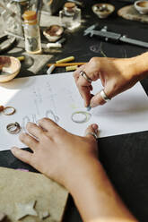 Die Hände eines Juweliers skizzieren einen Ringentwurf auf Papier an der Werkbank - DSHF00621