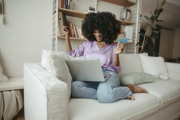 Glückliche Frau mit Kreditkarte beim Online-Shopping auf dem Laptop zu Hause - RCPF01597