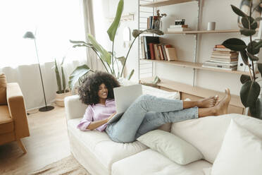 Woman using laptop lying comfortably on sofa in living room - RCPF01600