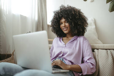 Lächelnde Afro-Frau mit Laptop zu Hause - RCPF01608