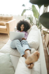 Young woman using laptop lying on sofa in living room - RCPF01611