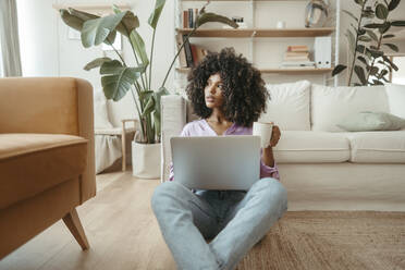 Kontemplative Frau mit Kaffeetasse und Laptop zu Hause - RCPF01614