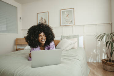 Afro woman using laptop on bed at home - RCPF01622