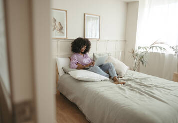 Junge Frau mit Laptop auf dem Bett im Schlafzimmer sitzend - RCPF01626
