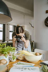 Junge Food-Stylistin beim Fotografieren durch eine Digitalkamera im Studio - MASF33927