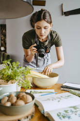Food stylist photographing vegetable bowl using digital camera in studio - MASF33931