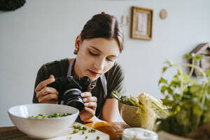 Food-Stylist justiert Kameraobjektiv beim Fotografieren von grünen Erbsen im Studio - MASF33932