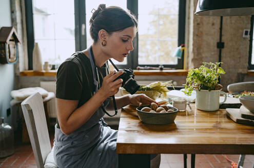 Seitenansicht eines Food-Stylisten, der Pilze in einer Schale durch eine Digitalkamera im Studio fotografiert - MASF33934