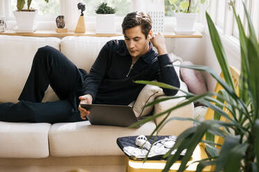 Young male freelancer watching laptop while lying on sofa at home - MASF33945