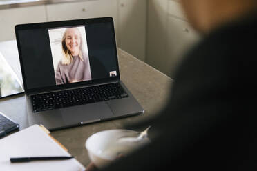 Businesswoman talking with businessman through video call on laptop at home - MASF33954