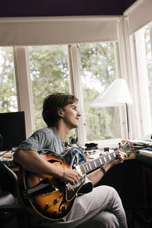 Seitenansicht eines Mannes, der zu Hause sitzend Gitarre übt - MASF33976