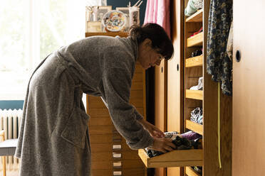 Woman wearing bathrobe searching in wardrobe drawer at home - MASF33980