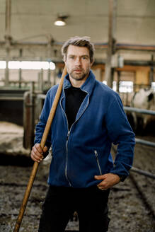 Farmer standing with wooden stick at cattle farm - MASF34013