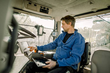 Landwirt bedient Computer im Traktor sitzend auf dem Bauernhof - MASF34025
