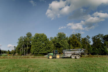 Traktor auf einem Feld gegen einen Baum unter bewölktem Himmel - MASF34028