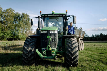 Landwirt steht auf einem Traktor auf einem Feld unter Himmel - MASF34030