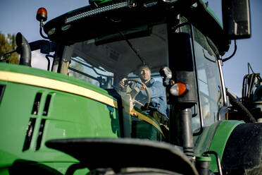 Niedriger Blickwinkel auf einen reifen Landwirt, der an einem sonnigen Tag Traktor fährt - MASF34033