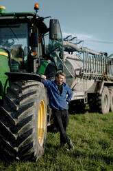 Glücklicher reifer Landwirt mit Traktor auf dem Feld stehend - MASF34034