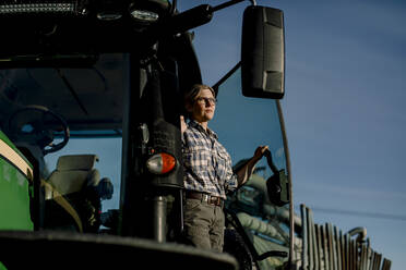Nachdenklicher Landwirt auf einem Traktor stehend auf einem Bauernhof - MASF34046