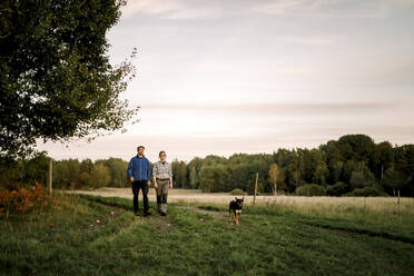 Ältere Landwirte mit Hund gehen bei Sonnenuntergang auf einem Feld spazieren - MASF34075