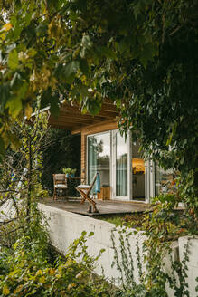 Stühle auf einer Holzveranda inmitten von Pflanzen vor dem Haus - MASF34085