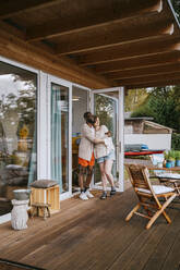 Multiracial couple embracing each other while standing on porch near doorway - MASF34098