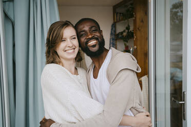 Glückliches multirassisches Paar, das sich an der Tür umarmt - MASF34109
