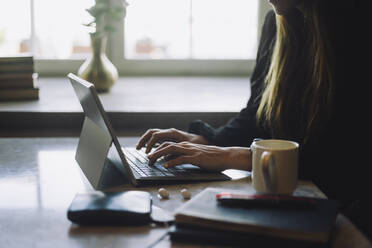 Hands of female entrepreneur typing on laptop at table in restaurant - MASF34146