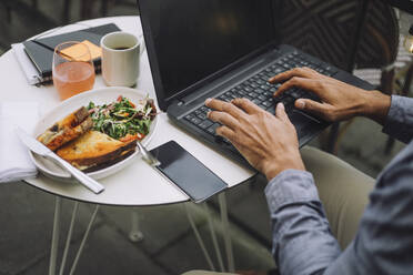 Hands of businessman using laptop by meal and smart phone on table - MASF34151