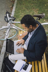 Male professional using laptop while sitting on bench - MASF34167