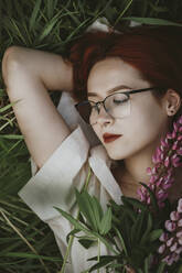 Redhead girl lying on grass with lupin flowers - IEF00267