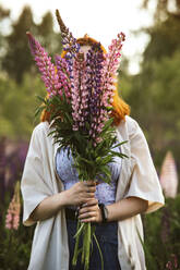 Teenage girl covering face with lupin flowers - IEF00278