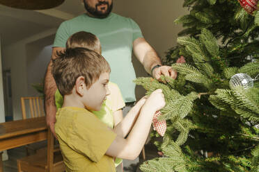 Father assisting sons to decorate Christmas tree at home - OSF01197