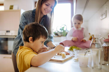 Eine Mutter von zwei kleinen Kindern bereitet das Frühstück in der Küche zu Hause vor. - HPIF03226