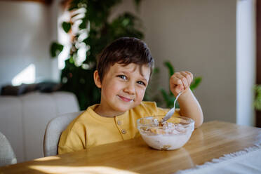 Das Porträt eines lächelnden Jungen, der zu Hause in der Küche sein Frühstück genießt - HPIF03231