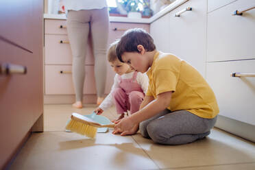 A little boy and girl helping to clean house using pan and brush as they sweep up dirt off floor. - HPIF03237