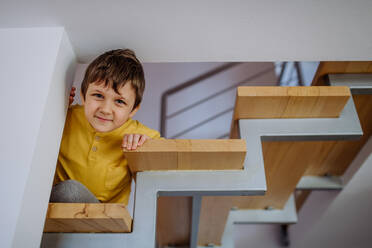 Ein kleiner Junge versteckt sich auf einer Holztreppe und schaut auf sein Zuhause hinunter - HPIF03241