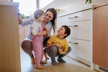A young cheerful mother playing with her little children and having fun in kitchen. - HPIF03247