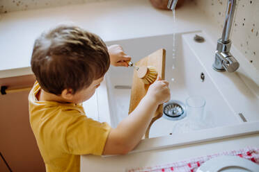 Ein kleiner Junge wäscht Tasse in der Spüle in der Küche mit hölzernen schrubben, nachhaltige lifestlye. - HPIF03250