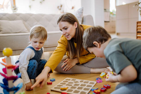 Junge Mutter und Kinder spielen mit Montessori-Holzspielzeug im Wohnzimmer und verbringen eine schöne Familienzeit miteinander. - HPIF03264