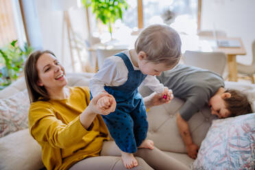 Eine junge, fröhliche Mutter spielt mit ihren kleinen Kindern und hat Spaß, wenn sie sie auf das Sofa hebt. - HPIF03273