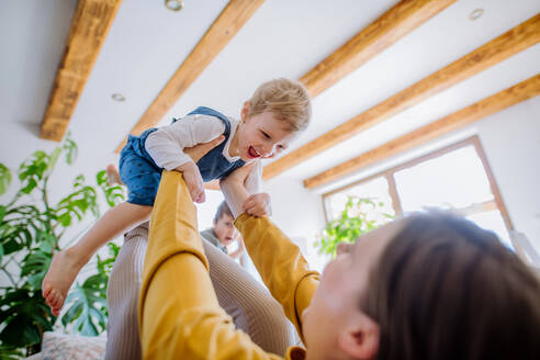 Eine junge, fröhliche Mutter spielt mit ihren kleinen Kindern und hat Spaß, wenn sie sie auf das Sofa hebt. - HPIF03274