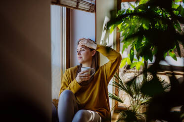A portrait of happy young woman resting and daydreaming at home, shot through window. - HPIF03282