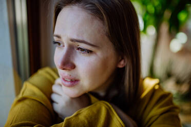 Junge Frau, die zu Hause unter Depressionen leidet, weint und aus dem Fenster schaut. - HPIF03288