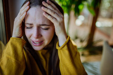 Eine Frau, die unter Depressionen leidet und zu Hause weint, hält den Kopf in den Händen. - HPIF03289